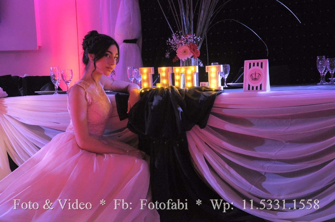 Quinceañera sentada en la mesa principal con luces rosas y letras luminosas